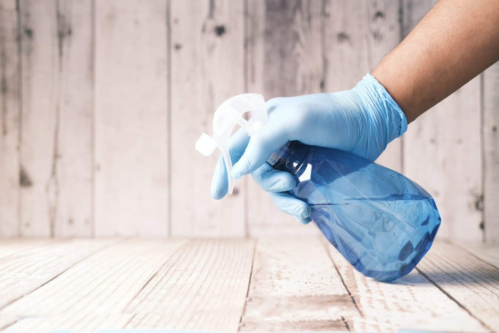 Gloved hand holding a spray bottle over a clean surface